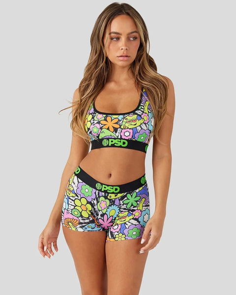 Woman wearing a two-piece set with colorful floral print and black PSD waistband details on sports bra and shorts.