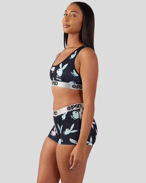 Woman wearing black Playboy sports bra and shorts with white bunny logo print and gray waistband.