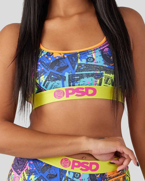Colorful sports bra with blue, yellow, and purple dollar bill print and yellow PSD waistband on model with long dark hair.