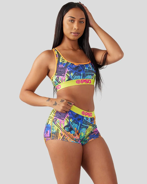 Woman wearing a colorful dollar-print sports bra and matching shorts with neon yellow trim and branding.