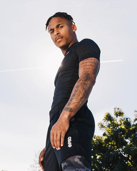 Black short-sleeve compression tee with fitted design, shown on model in side profile outdoors.