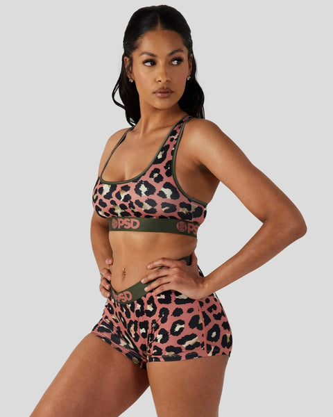 Woman wearing pink and black leopard print sports bra and shorts with olive green PSD waistbands.