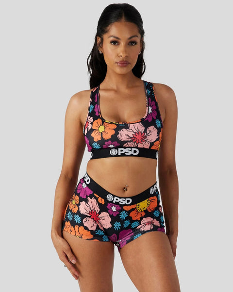 Woman wearing black sports bra and boy shorts with multicolored floral print and PSD branding.