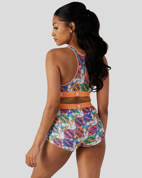 Playboy Geo two-piece swimsuit with colorful geometric pattern, orange trim, and matching swim skirt shown from back.
