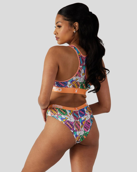 Woman wearing colorful geometric patterned sports bra and briefs set with orange trim in back view.