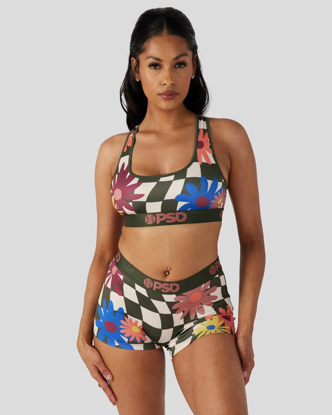 Woman wearing a colorful floral and checkered sports bra and matching boy shorts set with green trim and PSD branding.