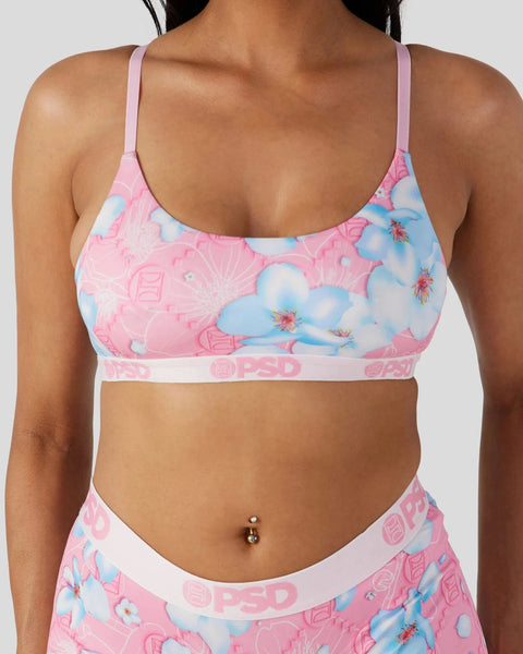 Pink sports bra with blue floral and cloud pattern, thin straps, white elastic band with branding.