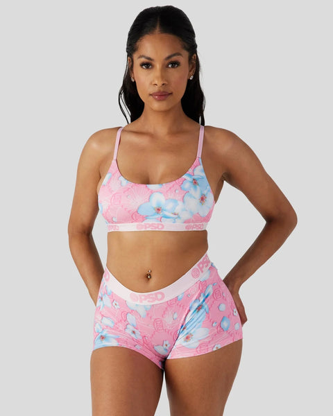 Woman wearing pink and blue floral sports bra and matching shorts set against neutral background.