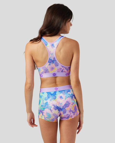 Woman wearing purple floral sports bra and matching shorts with blue and yellow butterfly and flower print.