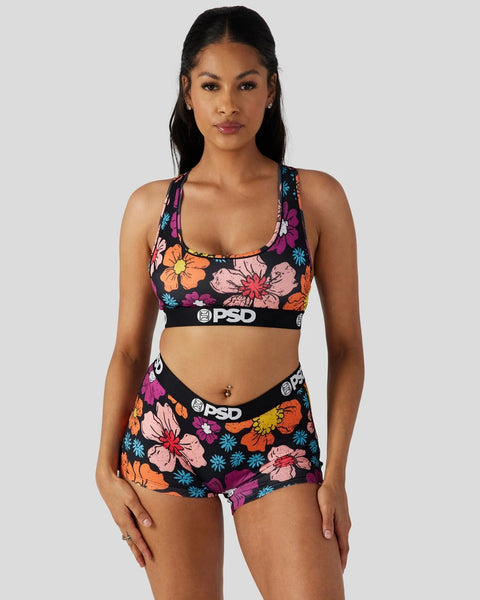 Woman wearing black sports bra and shorts with colorful floral print and PSD waistband.