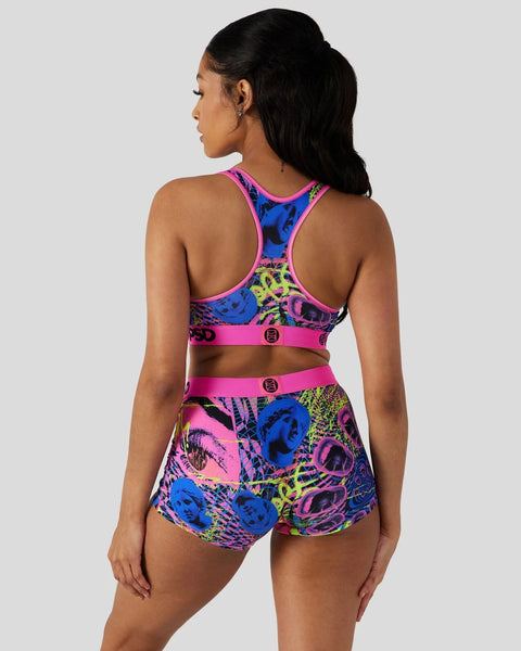 Woman wearing neon colorful grid-patterned sports bra and shorts set with pink trim and logo details, shown from back.