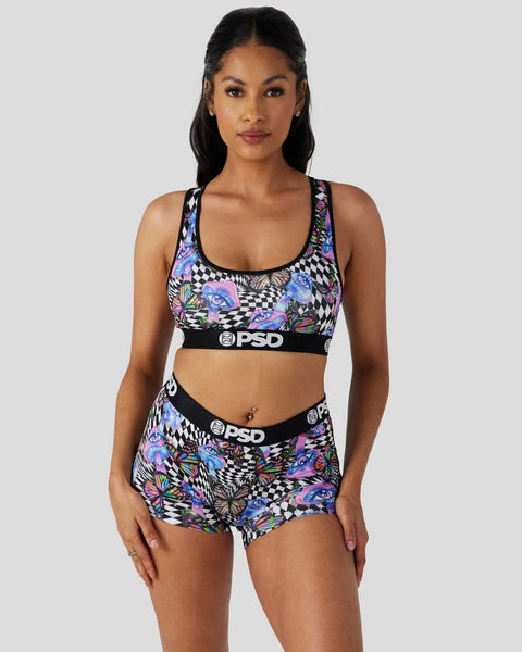 Woman wearing colorful patterned sports bra and shorts with black PSD waistband and checkered design.