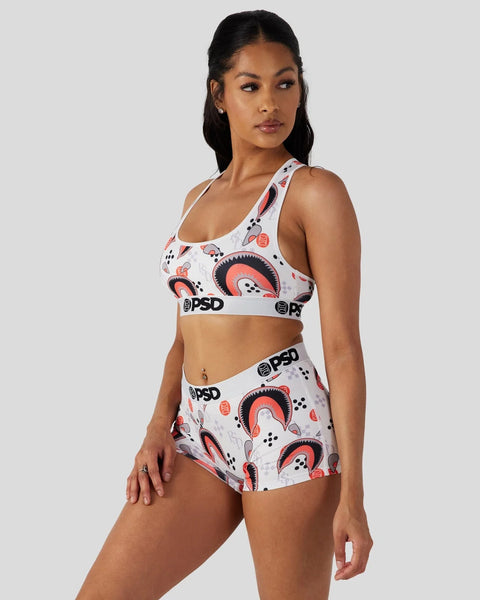 Woman wearing white sports bra and shorts with red and navy abstract geometric pattern and PSD branding.