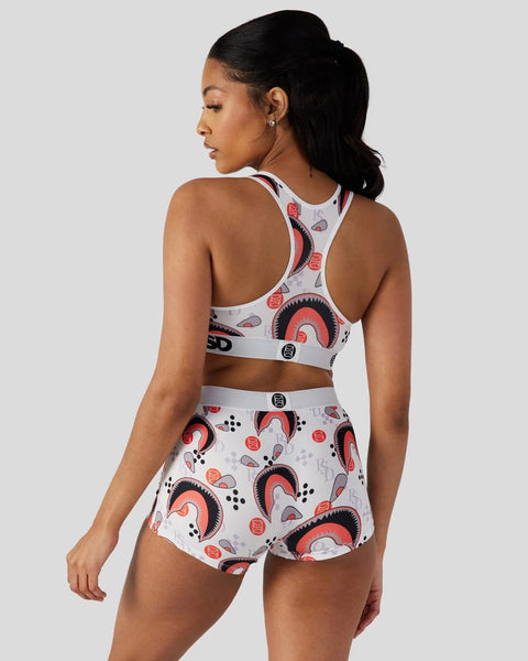 Woman wearing white sports bra and shorts set with red and black abstract circular pattern design.
