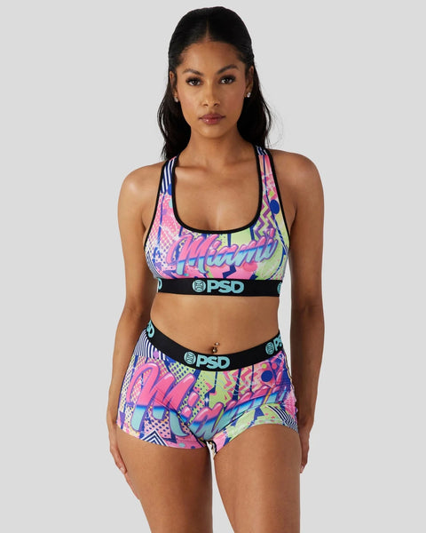 Woman wearing colorful geometric patterned sports bra and matching shorts with black PSD waistbands.