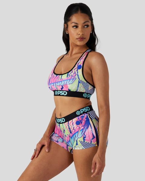 Woman wearing neon pink and blue patterned sports bra and matching shorts with black PSD waistbands.