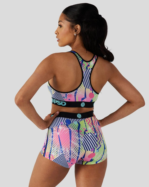 Woman wearing colorful geometric patterned sports bra and matching shorts with black trim and logo details.