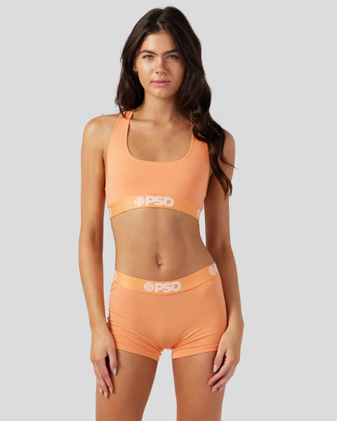 Woman wearing coral-colored sports bra and matching shorts with PSD branding on waistband and underband.
