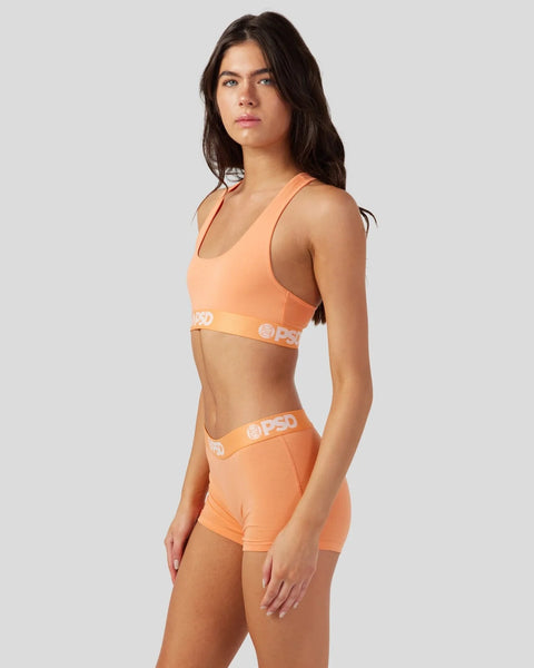 Woman wearing coral sleeveless bra top and matching shorts with white waistband logos.