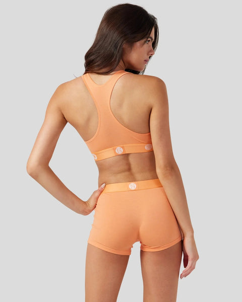 Coral racerback sports bra and shorts set with logo buttons, shown from back view on model.