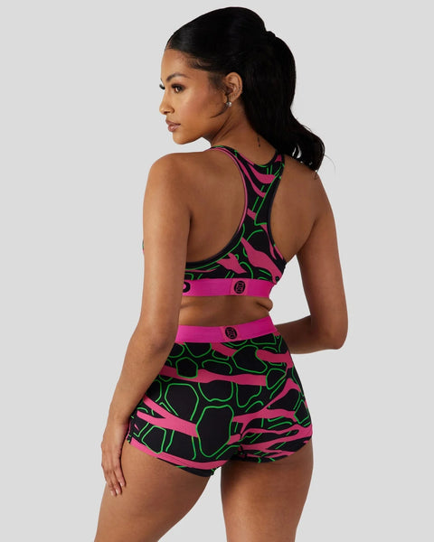 Neon pink and green giraffe-print sports bra and shorts set with black accents, shown on model from back view.
