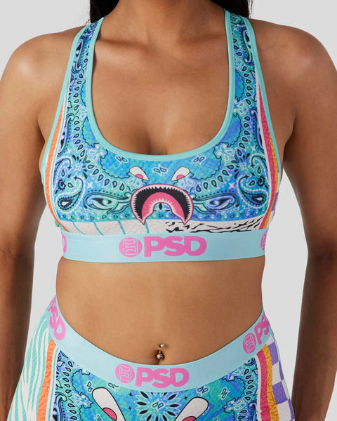 Light blue sports bra with colorful paisley and eye pattern, rainbow side stripes, and pink PSD waistband.