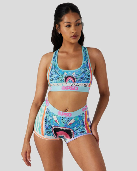 Woman wearing turquoise sports bra and matching shorts with colorful graphic print and PSD branding.