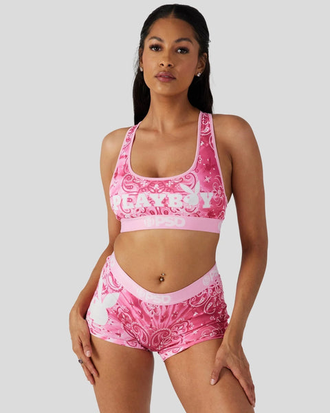 Woman wearing pink Playboy-branded sports bra and matching shorts with paisley print pattern.