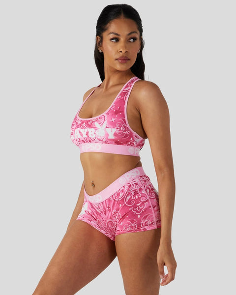 Pink patterned sports bra and shorts set with ornamental design worn by model against neutral background.