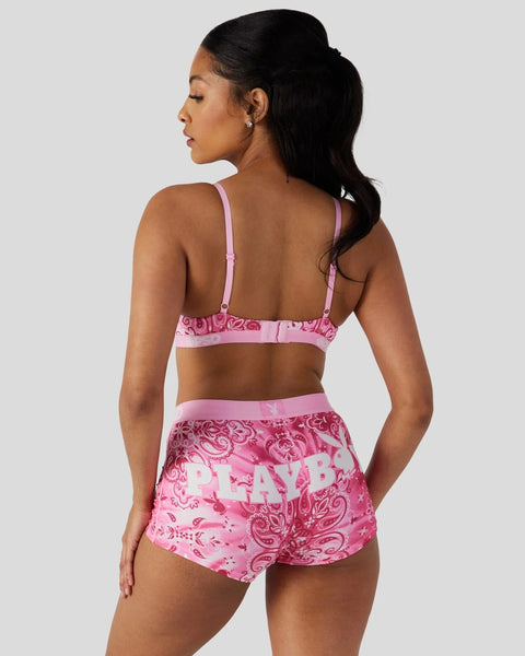 Woman wearing pink Playboy lingerie set with paisley pattern and logo, shown from back.
