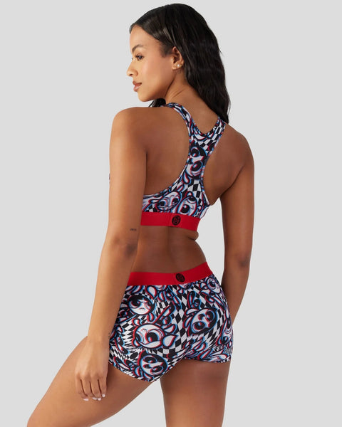 Woman wearing a two-piece athletic set with red and blue abstract patterned racerback top and matching shorts with red waistb