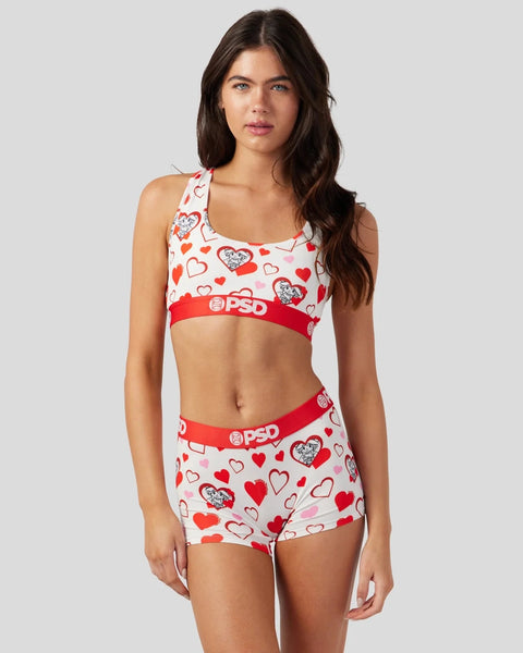 White sports bra and shorts set with red and pink heart print and red elastic waistbands.