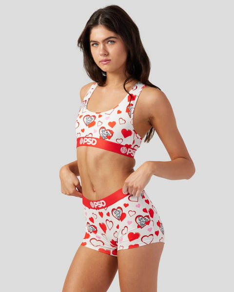 White sports bra and shorts set with red and pink heart print and red elastic bands.