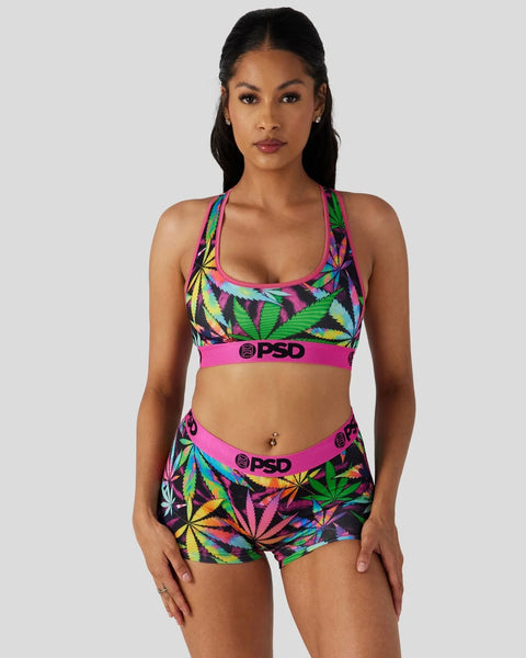 Woman wearing colorful leaf-print sports bra and matching boy shorts set with pink elastic bands.