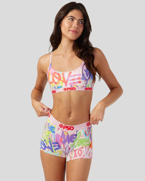 Woman wearing a colorful two-piece set with multicolor graffiti-style text print and red branded waistband.