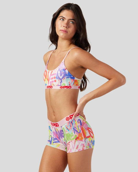 Woman wearing colorful graffiti-print sports bra and shorts set with pink PSD waistbands.