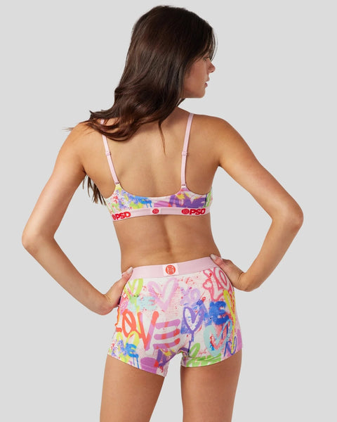Woman wearing colorful graffiti-print bra and shorts set with pink bands and red branding.