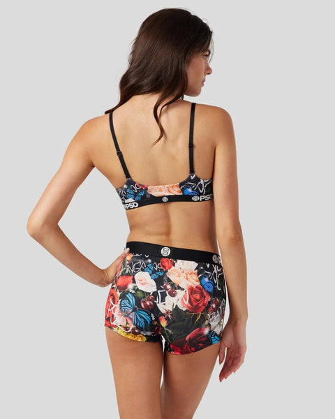 Woman wearing black sports bra and floral print shorts with multicolored flowers and blue butterflies, shown from back.