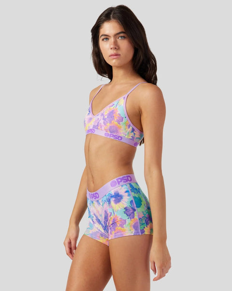 Woman wearing lavender sports bra and shorts with colorful floral print and purple waistband.