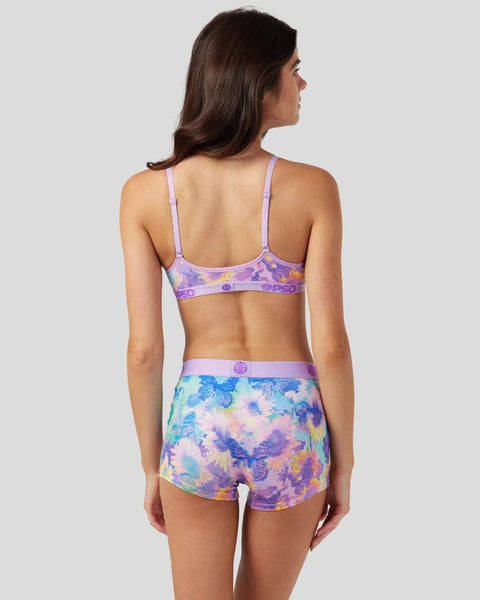 Woman wearing purple bralette and matching shorts with multicolored butterfly and floral print, shown from back.