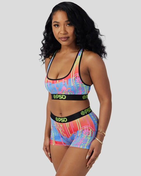 Woman wearing multicolored paisley-print sports bra and shorts set with black elastic bands labeled PSD.