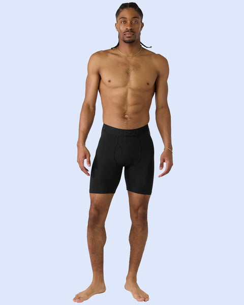 Man wearing black boxer briefs with fly opening against light blue background.