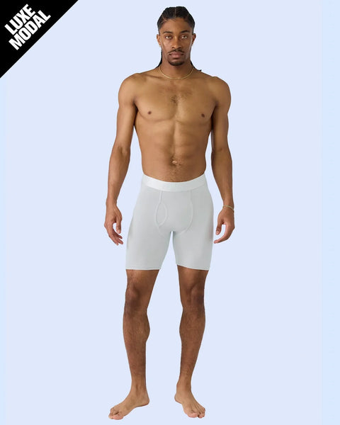 Man wearing white modal boxer shorts with elastic waistband, standing shirtless against light blue background.