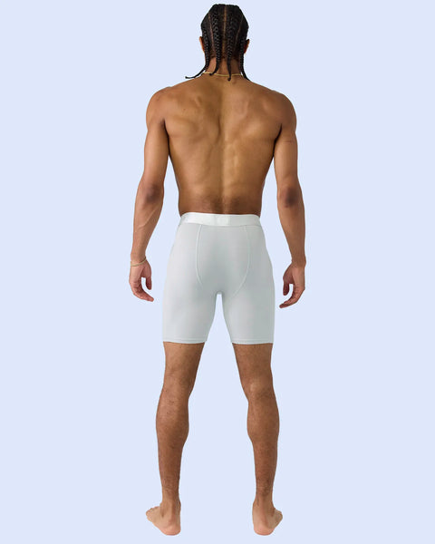 Man wearing white knee-length fitted shorts, shown from behind against a light blue background.