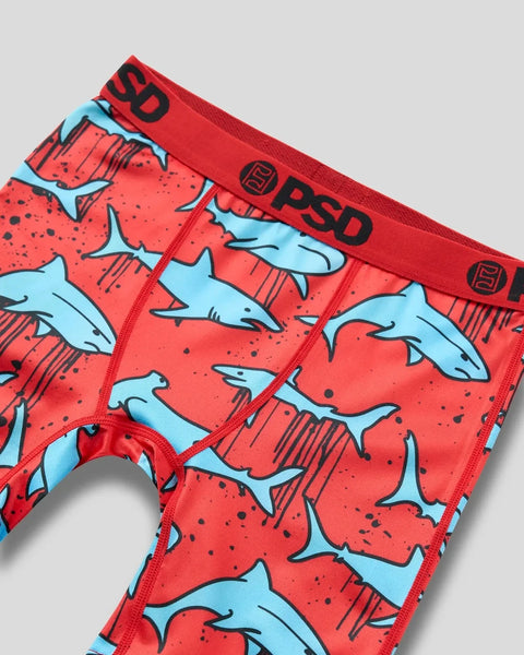 Red swim briefs with light blue shark pattern and black details, PSD branding on waistband.
