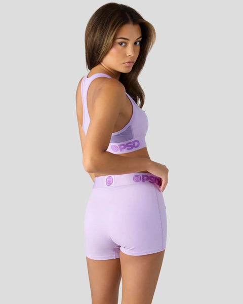 Woman wearing lavender sports bra and matching shorts with logo waistband, shown from back.