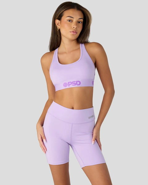 Lavender sports bra and bike shorts set with PSD branding on gray background.