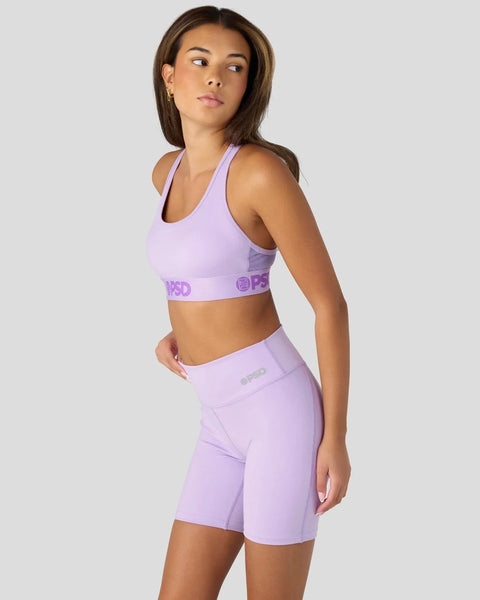 Woman wearing lavender sports bra and matching shorts with branded waistband detail.