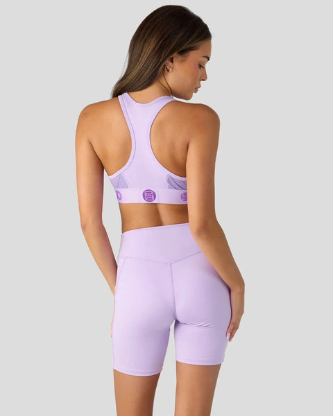 Woman wearing lavender sports bra and matching bike shorts with logo detail, shown from back view.