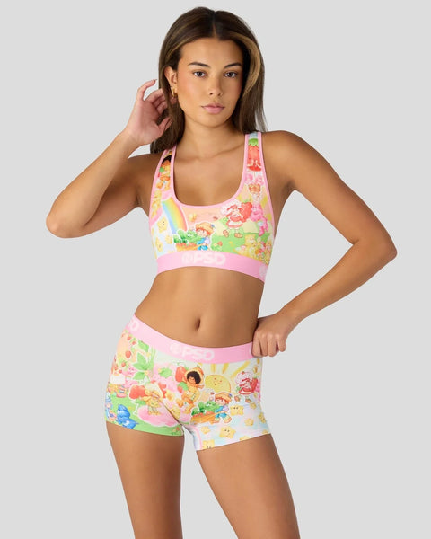 Woman wearing pink sports bra and shorts with colorful cartoon characters and fruit print design.